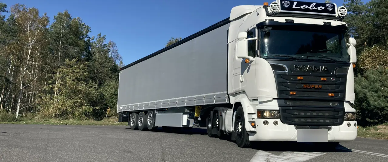 Ciągnik Scania z napisem Lobo i naczepą plandeką na tle lasu