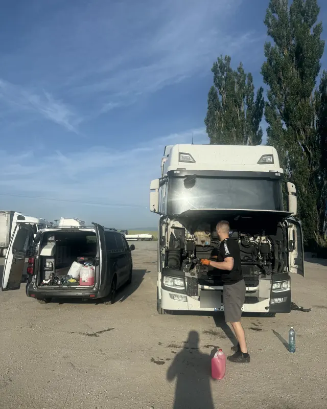 Mechanik naprawia ciągnik na placu, obok serwisowy bus